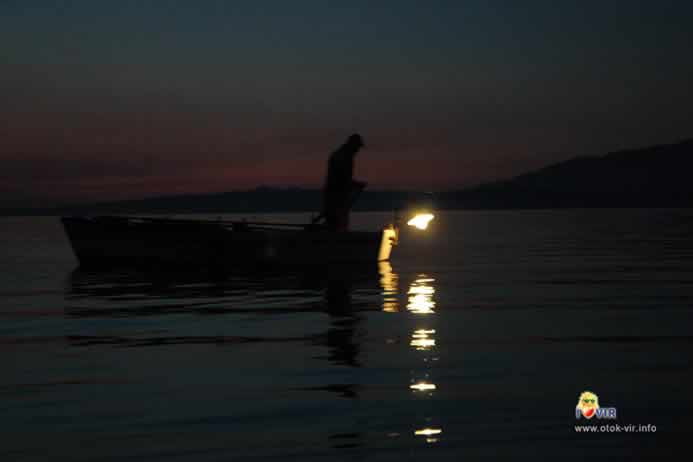 Ribar na drvenom brodu i lampom ribari po noći