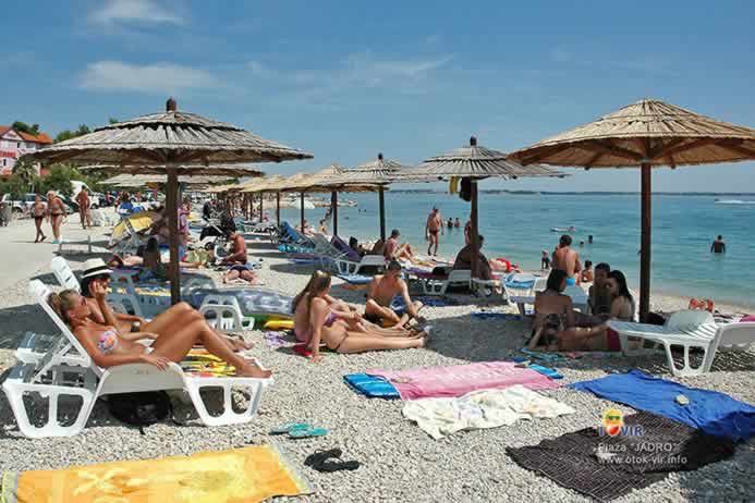 Turisti na plastičnim ležaljkama pod suncobranima na plaži Jadro