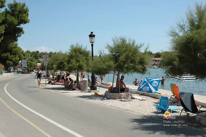 Tamarisi u betonskim žardinjerama za sunčanog dana ispred plaže Jadro s turistima