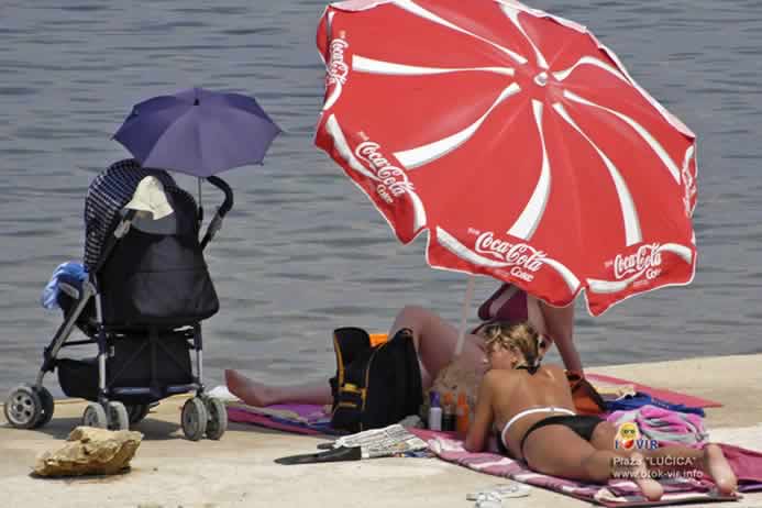 Veliki crveni suncobran sa znakom Coca Cole i zgodnom djevojkom koja leži na plaži