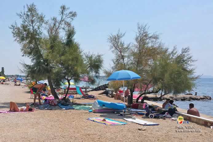 Turisti na plastičnim ležaljkama pod suncobranima na plaži Luka