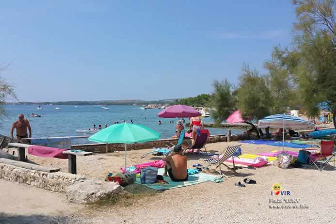 Kameno betonska plaža sa turistima suncobranima i kupačima