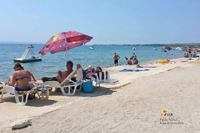 Turisti na bijelim plastičnim ležaljkama ispod suncobrana uživaju u sunčanom danu