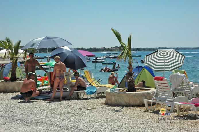 Turisti i ljetni rekviziti uz palme na šljunčanoj plaži