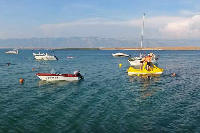 Turisti na zelenoj pedalini okruženi usidrenim gliserima i čamcima na moru