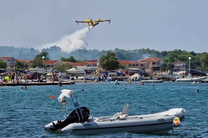 Turisti promatraju gašenje požara kanadera u blizini plaže s čamcima po danu